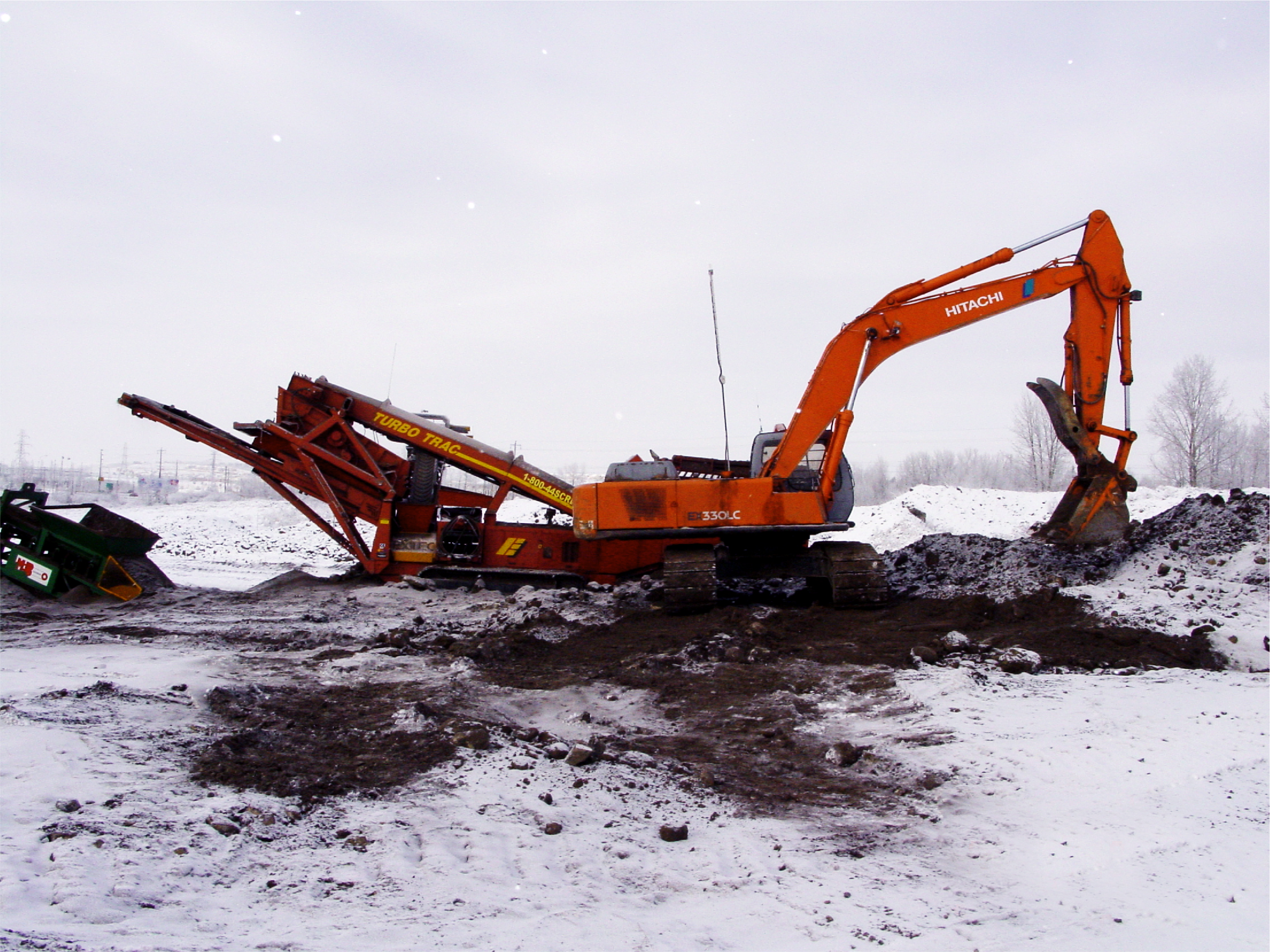 An Orange Hitachi Excavator operates in the snow to dig up soil